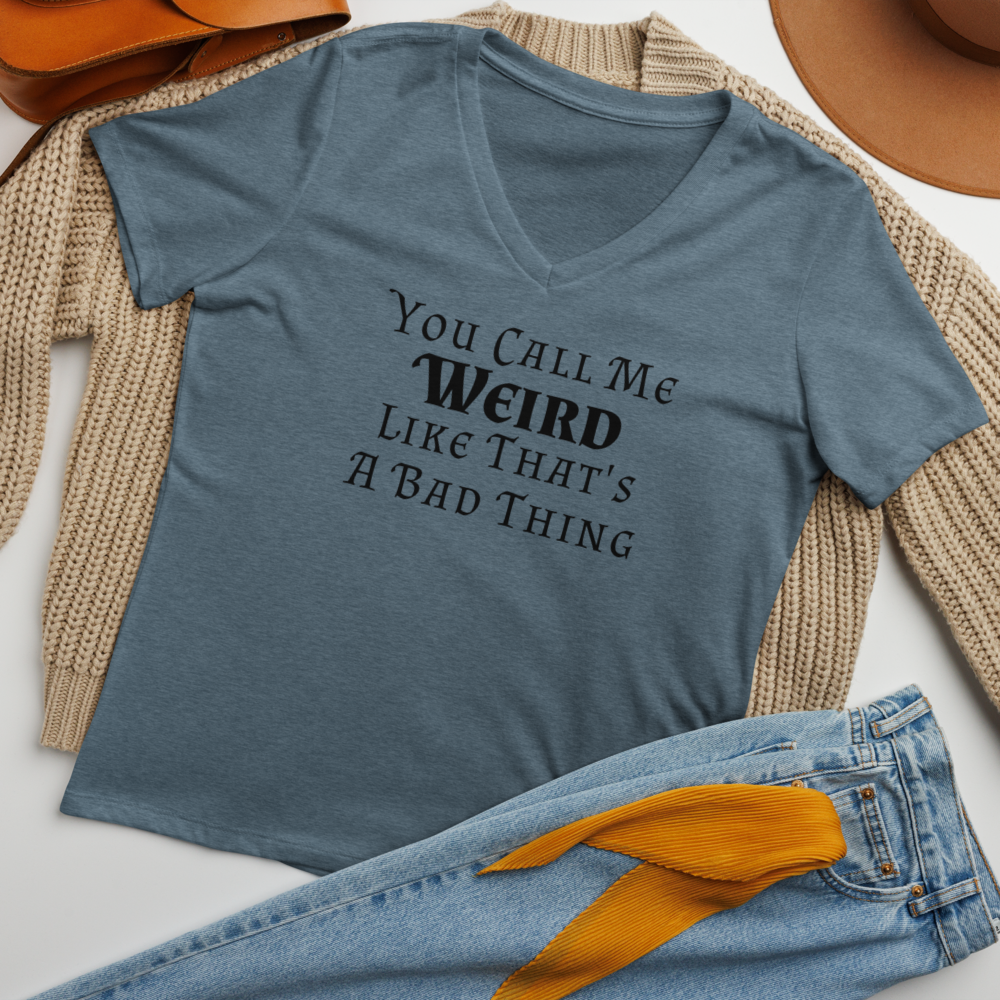 "You Call Me Weird Like That's A Bad Thing" printed on a heather slate women's relaxed v-neck t-shirt laying on a flat surface amongst other clothes