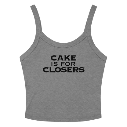 "Cake Is For Closers" printed on a athletic heather women's micro-rib tanktop laying on a flat surface amongst sunglasses and shorts