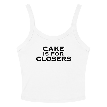 "Cake Is For Closers" printed on a solid white blend women's micro-rib tanktop laying on a flat surface amongst sunglasses and shorts