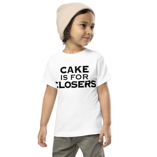"Cake Is For Closers" printed on a white toddler short sleeve tee worn by a male wearing a cap