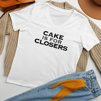 "Cake Is For Closers" printed on a solid white blend women's relaxed v-neck t-shirt laying on a flat surface amongst other clothes