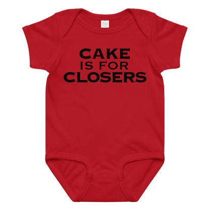 "Cake Is For Closers" printed on a red baby jersey bodysuit laying on a flat surface amongst other clothes