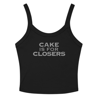 "Cake Is For Closers" printed on a solid black blend women's micro-rib tanktop laying on a flat surface amongst sunglasses and shorts