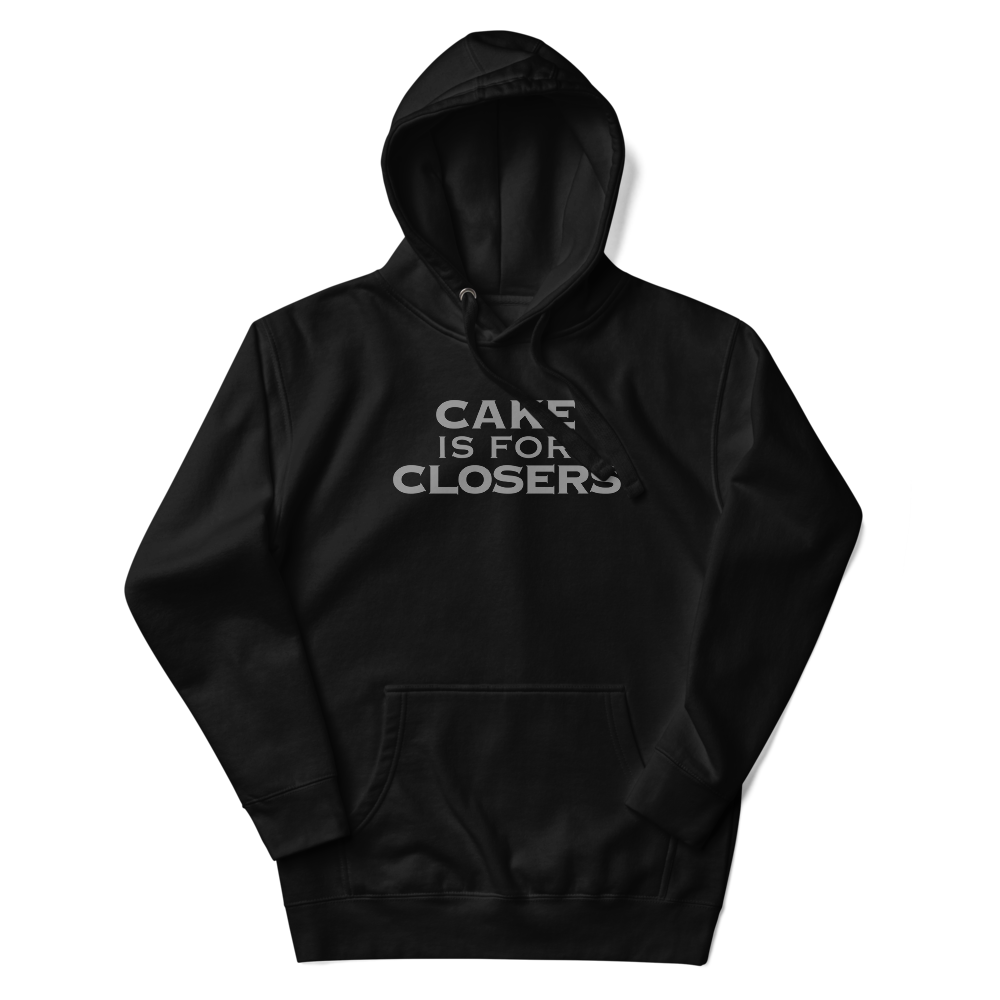 "Cake Is For Closers" printed on a black unisex hoodie laying on a flat surface with the hood up