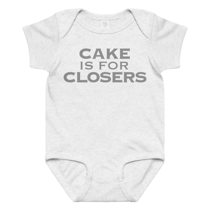 "Cake Is For Closers" printed on a ash baby jersey bodysuit laying on a flat surface amongst other clothes