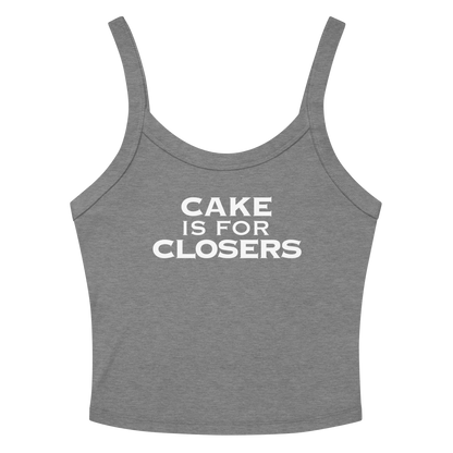 "Cake Is For Closers" printed on a athletic heather women's micro-rib tanktop laying on a flat surface amongst sunglasses and shorts
