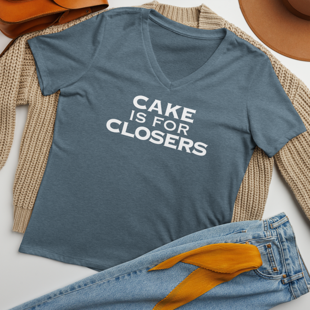 "Cake Is For Closers" printed on a heather slate women's relaxed v-neck t-shirt laying on a flat surface amongst other clothes