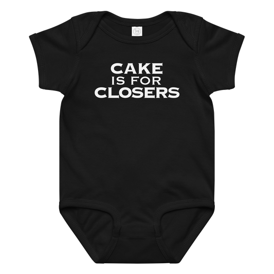"Cake Is For Closers" printed on a black baby jersey bodysuit laying on a flat surface amongst other clothes