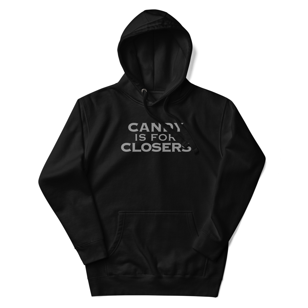 "Candy Is For Closers" printed on a black unisex hoodie laying on a flat surface with the hood up
