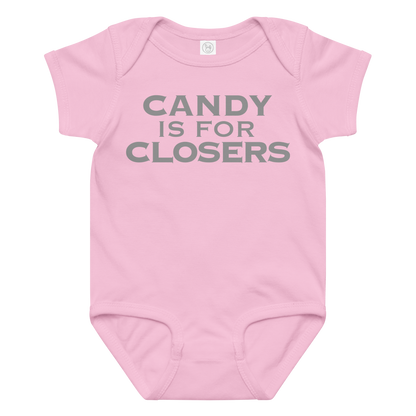 "Candy Is For Closers" printed on a pink baby jersey bodysuit laying on a flat surface amongst other clothes