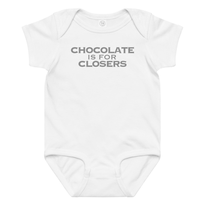 "Chocolate Is For Closers" printed on a white baby jersey bodysuit laying on a flat surface amongst other clothes