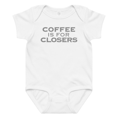 "Coffee Is For Closers" printed on a white baby jersey bodysuit laying on a flat surface amongst other clothes