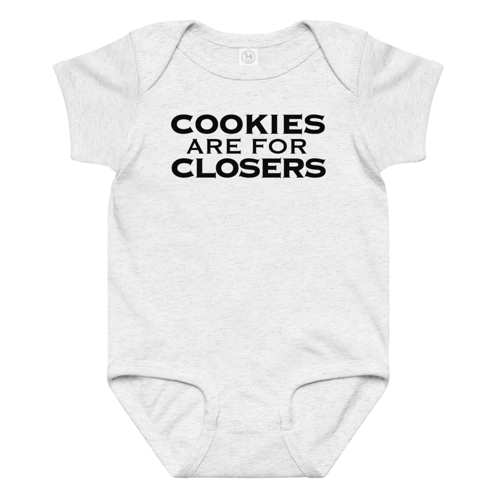 "Cookies Are For Closers" printed on a ash baby jersey bodysuit laying on a flat surface amongst other clothes