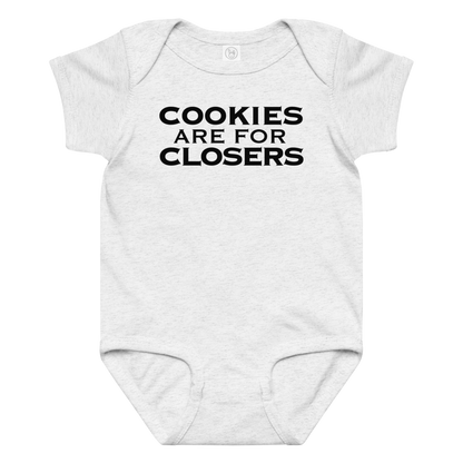 "Cookies Are For Closers" printed on a ash baby jersey bodysuit laying on a flat surface amongst other clothes