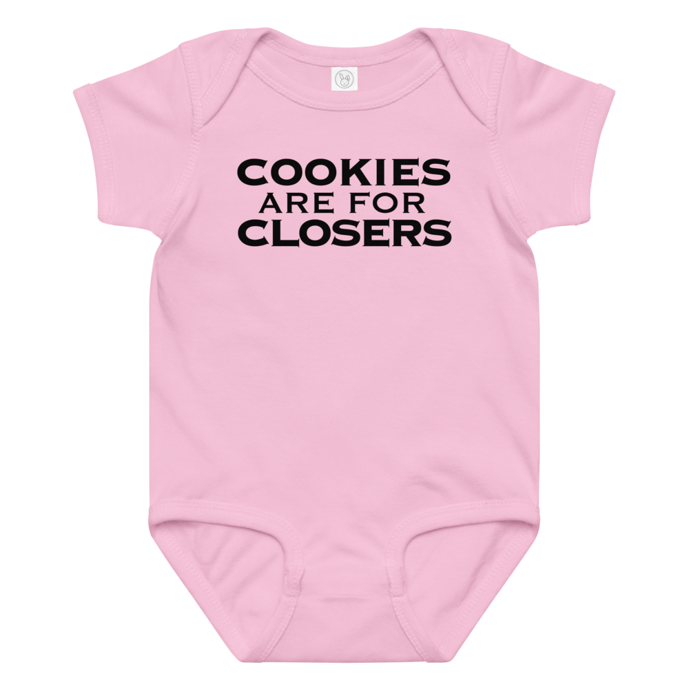 "Cookies Are For Closers" printed on a pink baby jersey bodysuit laying on a flat surface amongst other clothes
