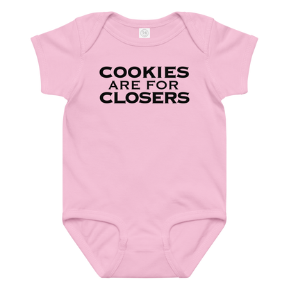 "Cookies Are For Closers" printed on a pink baby jersey bodysuit laying on a flat surface amongst other clothes