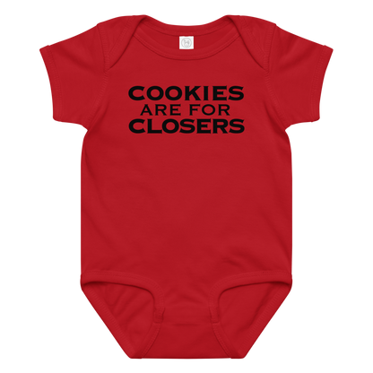 "Cookies Are For Closers" printed on a red baby jersey bodysuit laying on a flat surface amongst other clothes