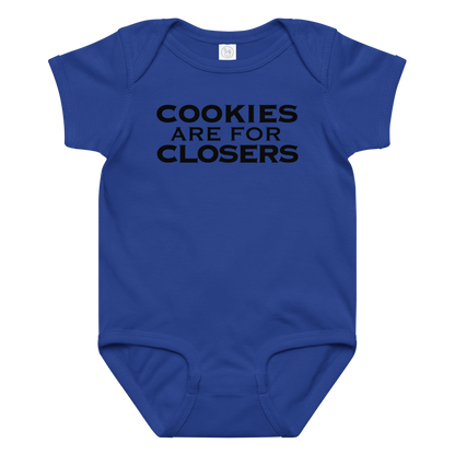 "Cookies Are For Closers" printed on a royal baby jersey bodysuit laying on a flat surface amongst other clothes