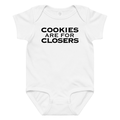 "Cookies Are For Closers" printed on a white baby jersey bodysuit laying on a flat surface amongst other clothes