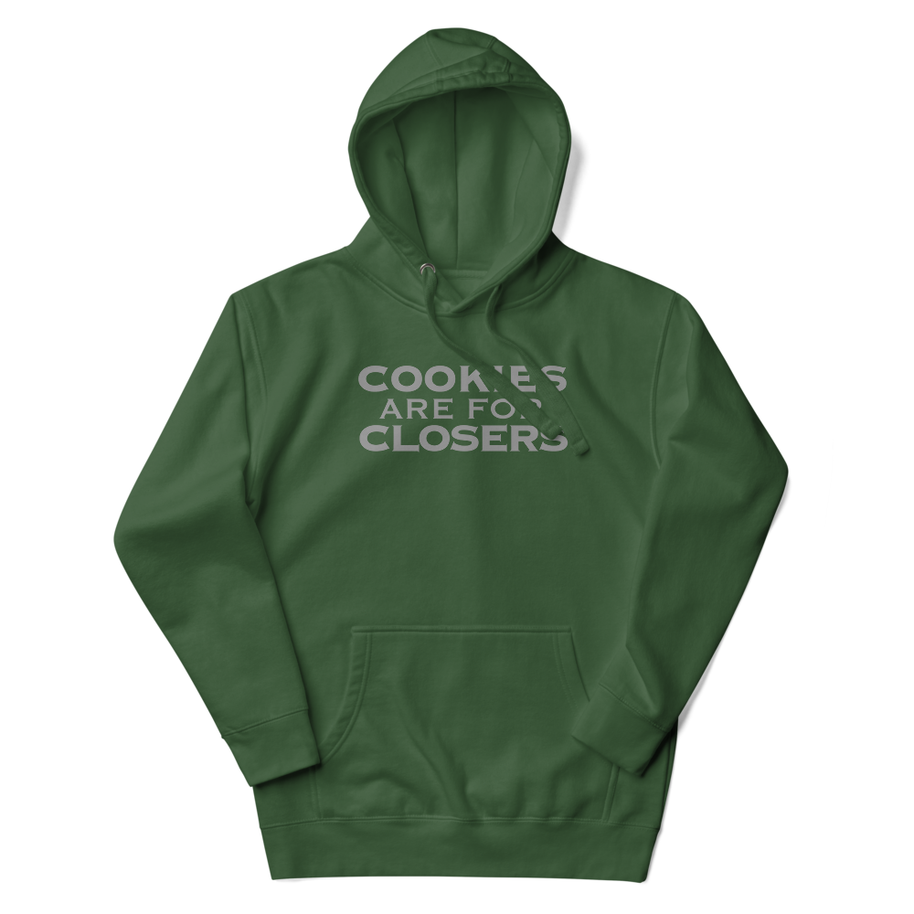 "Cookies Are For Closers" printed on a forest green unisex hoodie laying on a flat surface with the hood up
