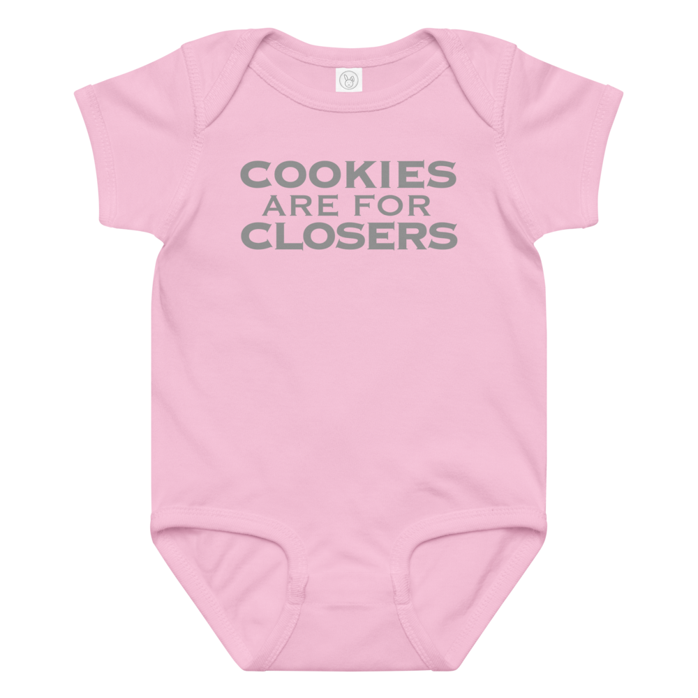 "Cookies Are For Closers" printed on a pink baby jersey bodysuit laying on a flat surface amongst other clothes