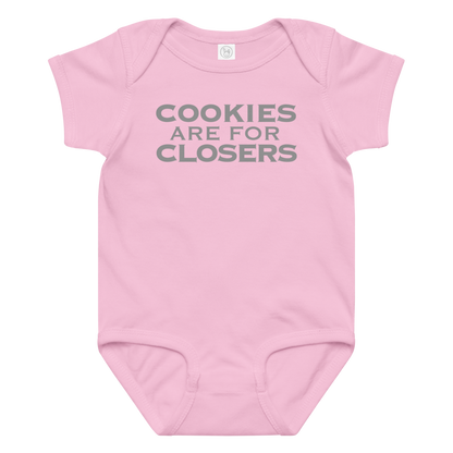 "Cookies Are For Closers" printed on a pink baby jersey bodysuit laying on a flat surface amongst other clothes