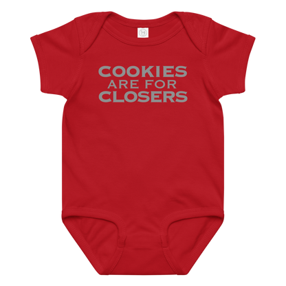 "Cookies Are For Closers" printed on a red baby jersey bodysuit laying on a flat surface amongst other clothes
