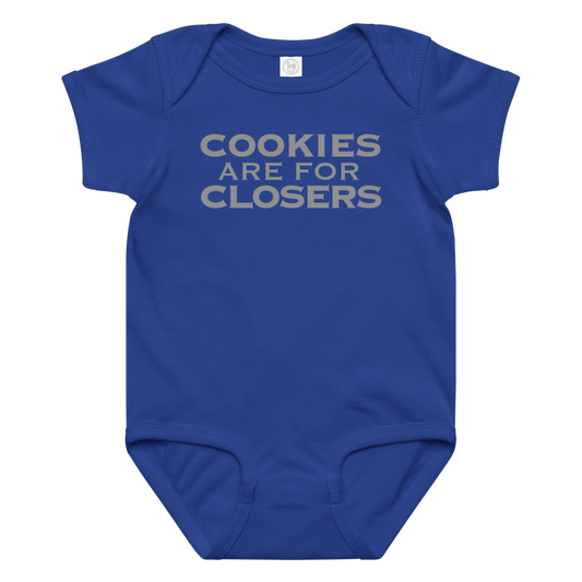 "Cookies Are For Closers" printed on a royal baby jersey bodysuit laying on a flat surface amongst other clothes