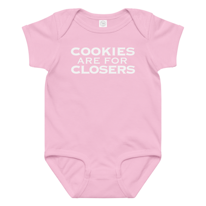 "Cookies Are For Closers" printed on a pink baby jersey bodysuit laying on a flat surface amongst other clothes