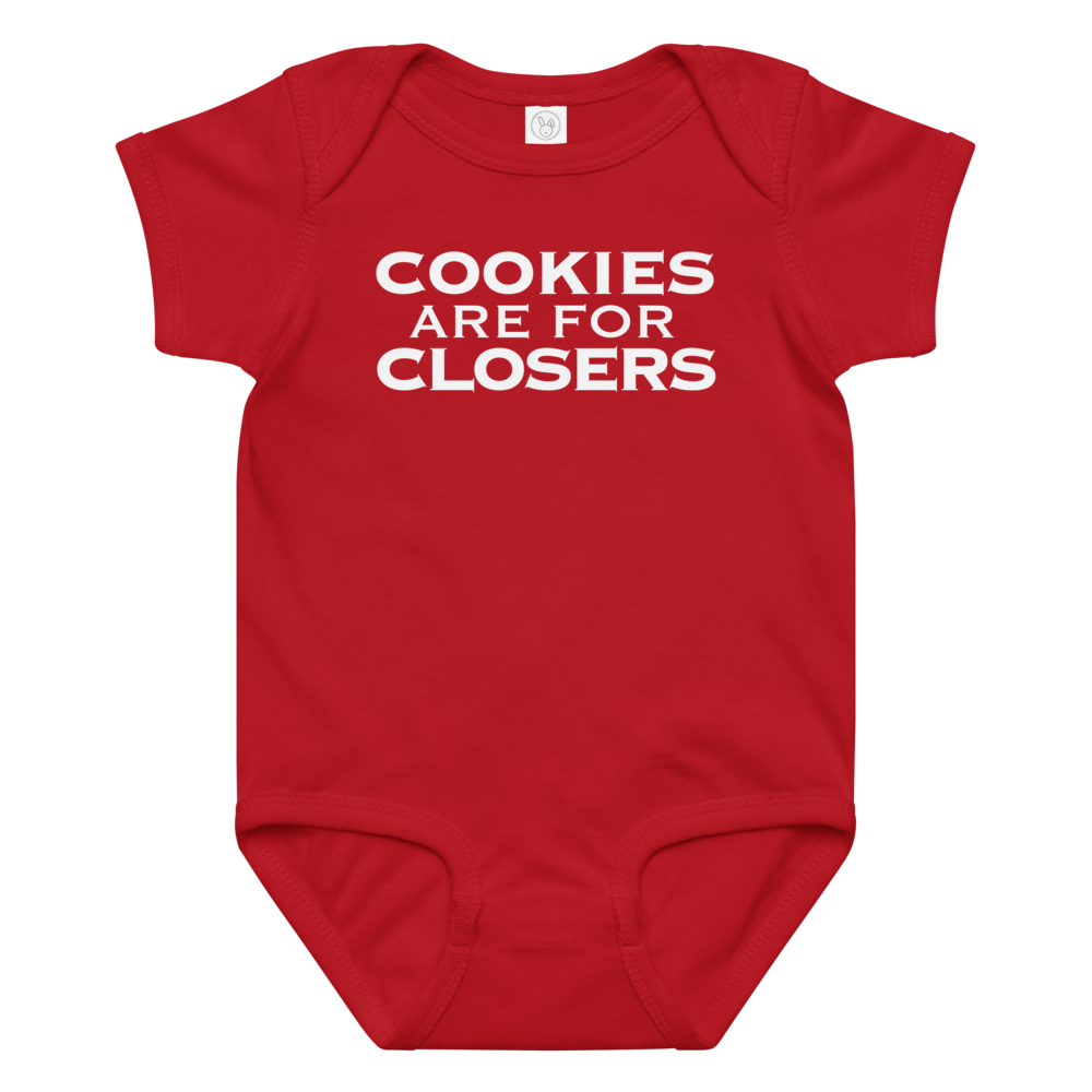"Cookies Are For Closers" printed on a red baby jersey bodysuit laying on a flat surface amongst other clothes
