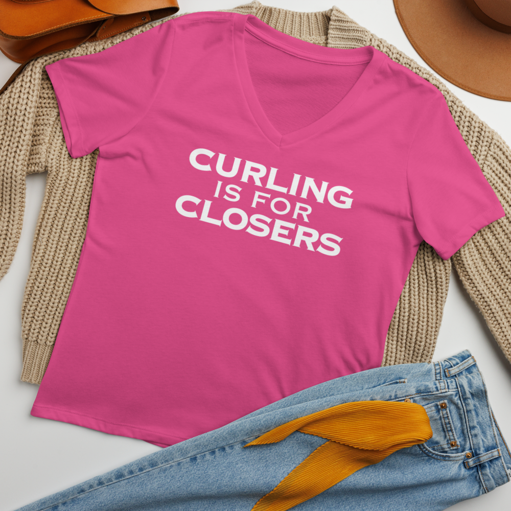 "Curling Is For Closers" printed on a berry women's relaxed v-neck t-shirt laying on a flat surface amongst other clothes