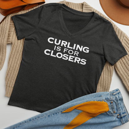 "Curling Is For Closers" printed on a dark grey heather women's relaxed v-neck t-shirt laying on a flat surface amongst other clothes