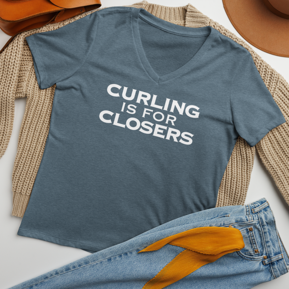 "Curling Is For Closers" printed on a heather slate women's relaxed v-neck t-shirt laying on a flat surface amongst other clothes