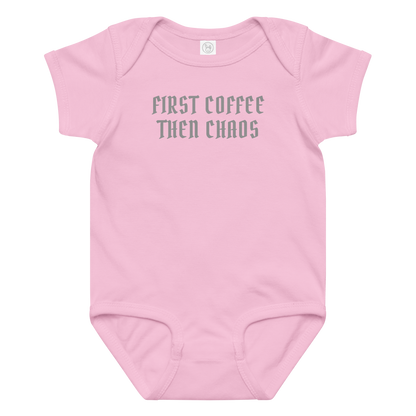 "First Coffee  Then Chaos" printed on a pink baby jersey bodysuit laying on a flat surface amongst other clothes