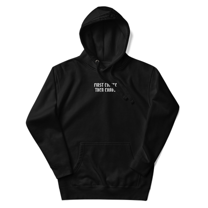 "First Coffee  Then Chaos" printed on a black unisex hoodie laying on a flat surface with the hood up