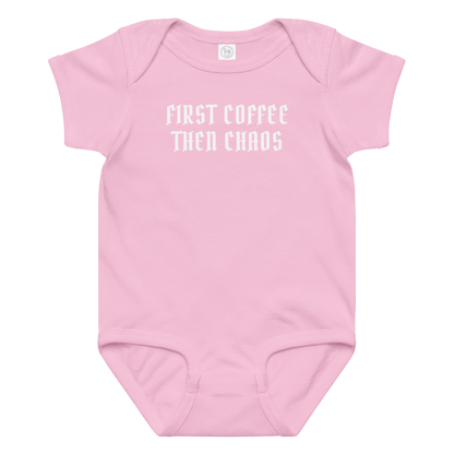 "First Coffee  Then Chaos" printed on a pink baby jersey bodysuit laying on a flat surface amongst other clothes