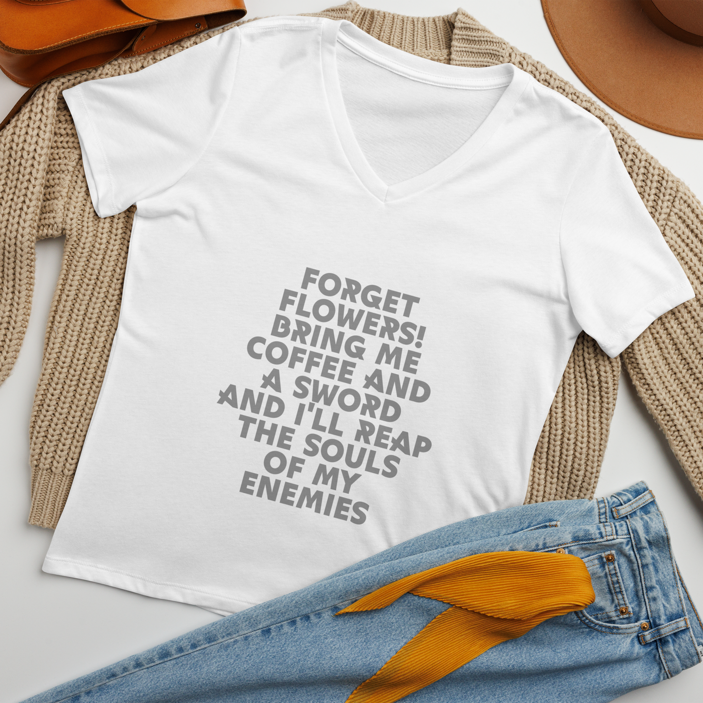 "Forget Flowers! Bring Me Coffee And A Sword And I'll Reap The Souls Of My Enemies" printed on a solid white blend women's relaxed v-neck t-shirt laying on a flat surface amongst other clothes