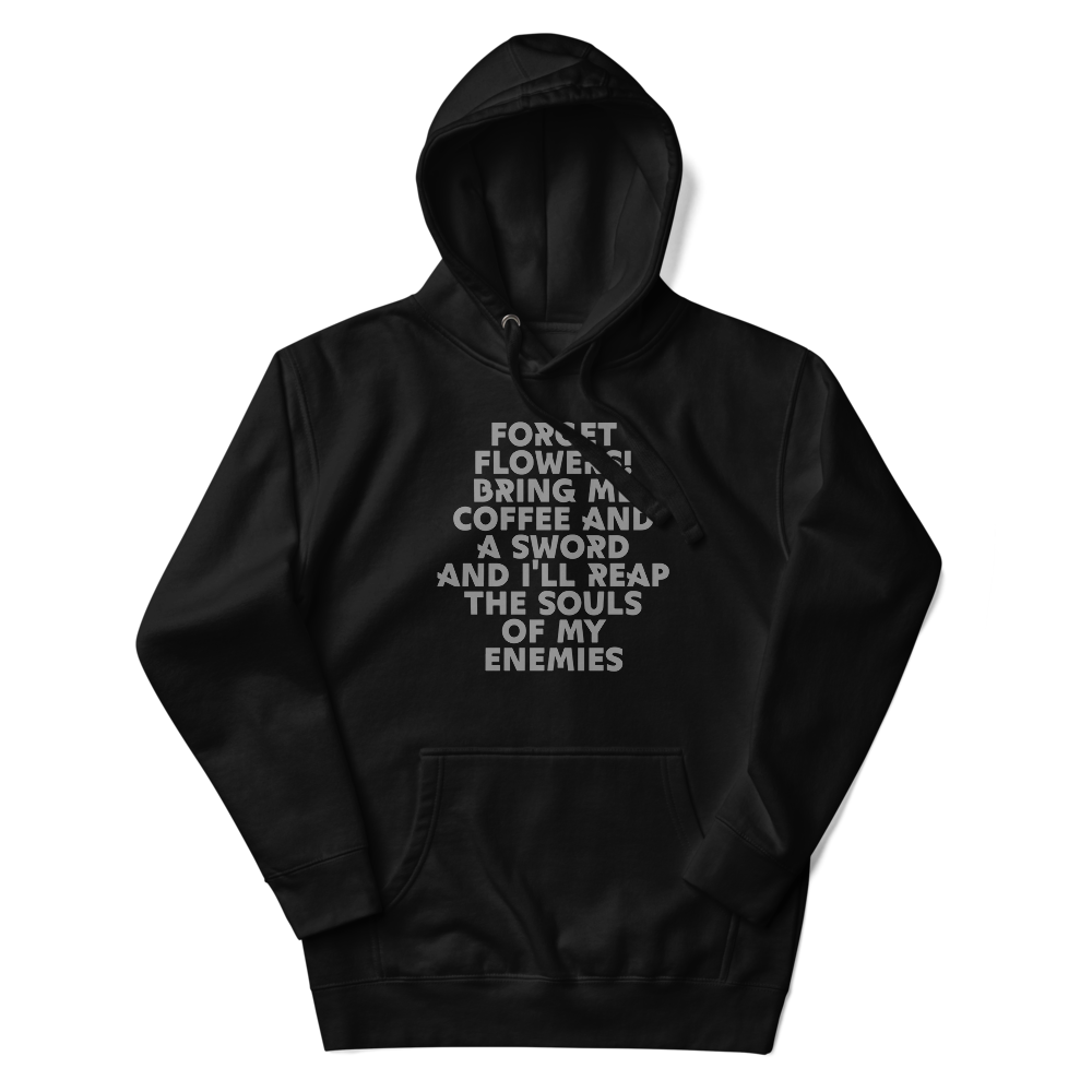 "Forget Flowers! Bring Me Coffee And A Sword And I'll Reap The Souls Of My Enemies" printed on a black unisex hoodie laying on a flat surface with the hood up