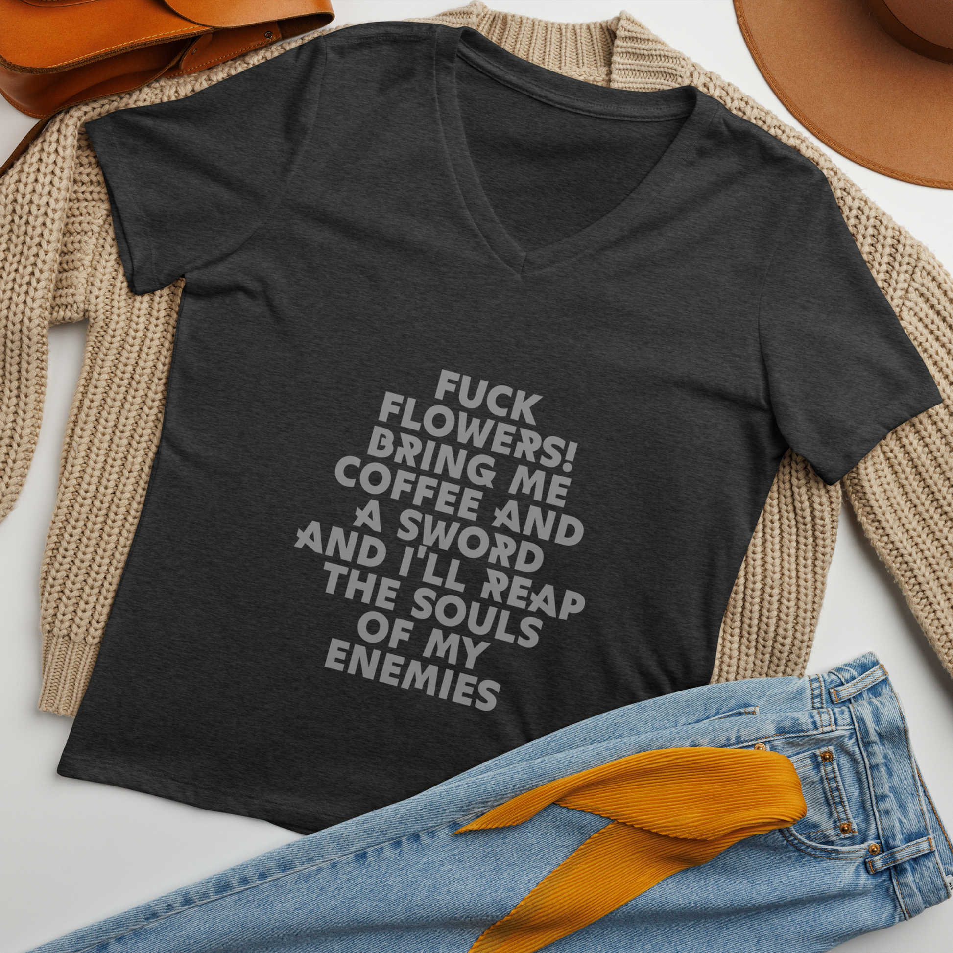 "Fuck Flowers! Bring Me Coffee And A Sword And I'll Reap The Souls Of My Enemies" printed on a dark grey heather women's relaxed v-neck t-shirt laying on a flat surface amongst other clothes