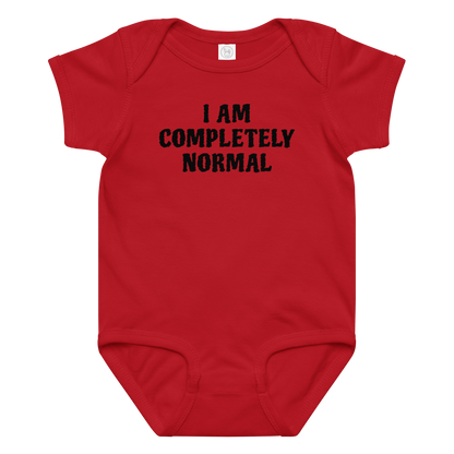 "I am completely normal" printed on a red baby jersey bodysuit laying on a flat surface amongst other clothes