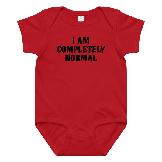 "I am completely normal" printed on a red baby jersey bodysuit laying on a flat surface amongst other clothes