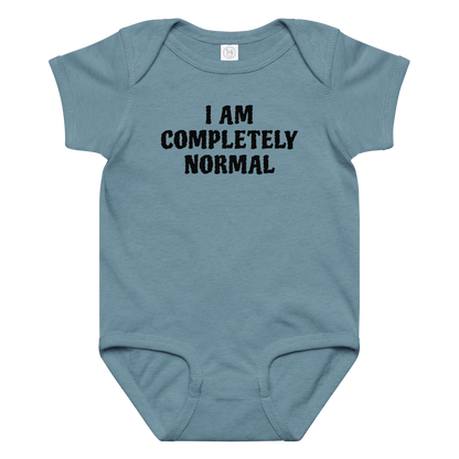 "I am completely normal" printed on a vintage indigo baby jersey bodysuit laying on a flat surface amongst other clothes