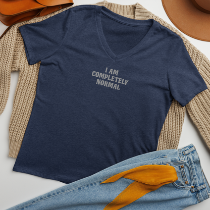 "I am completely normal" printed on a heather navy women's relaxed v-neck t-shirt laying on a flat surface amongst other clothes