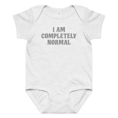 "I am completely normal" printed on a ash baby jersey bodysuit laying on a flat surface amongst other clothes