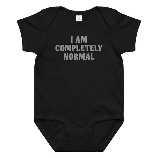 "I am completely normal" printed on a black baby jersey bodysuit laying on a flat surface amongst other clothes