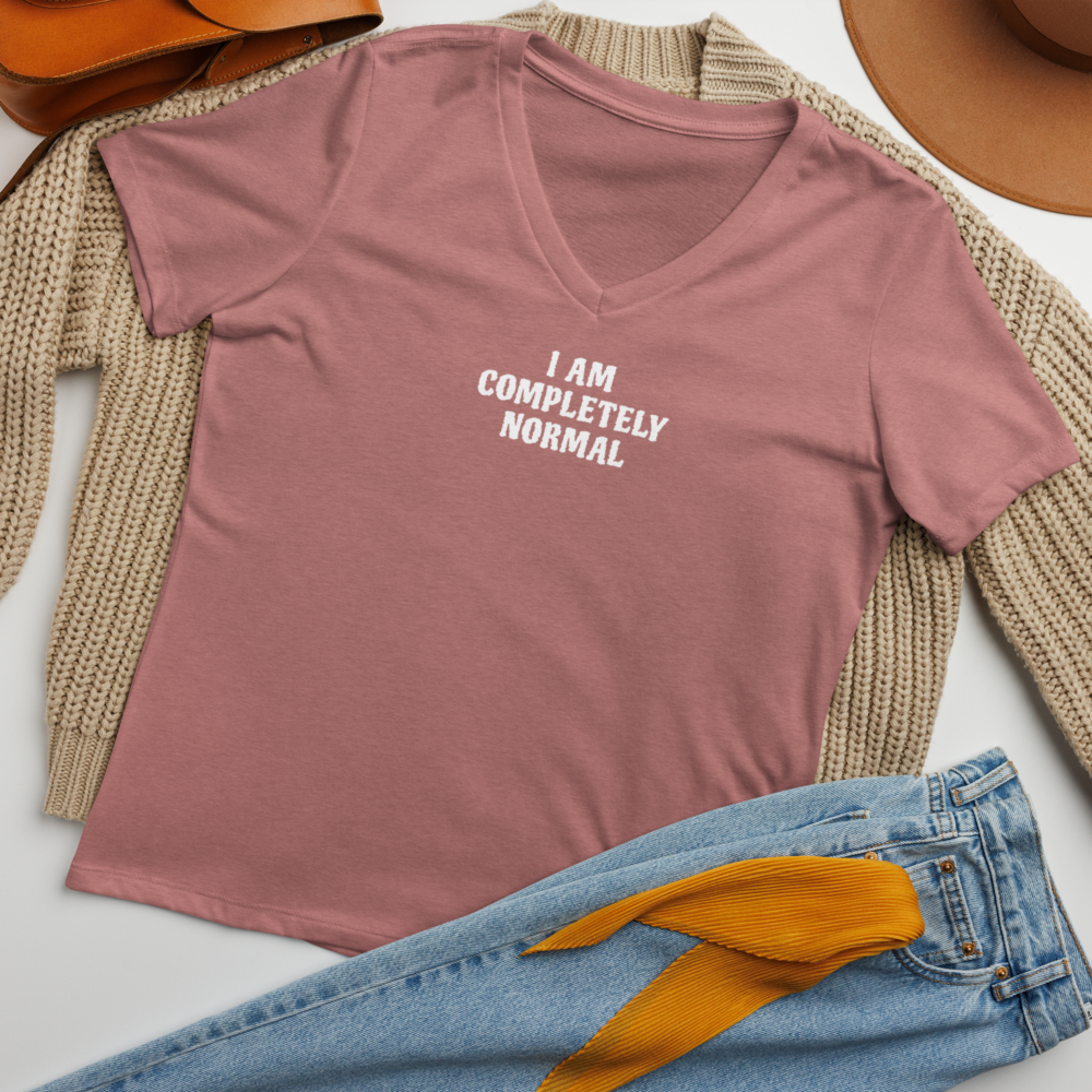 "I am completely normal" printed on a heather mauve women's relaxed v-neck t-shirt laying on a flat surface amongst other clothes
