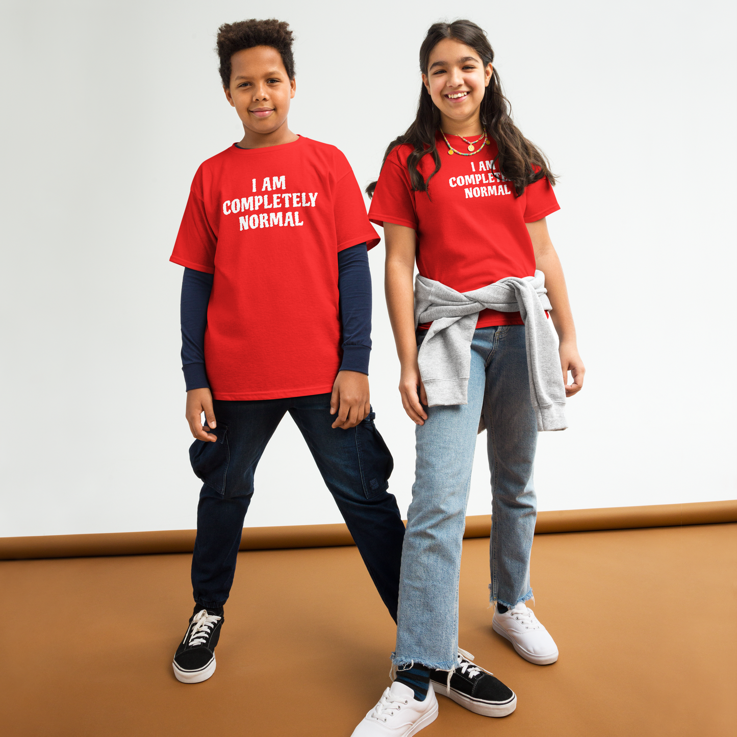 "I am completely normal" printed on a red youth classic tee worn by a female and male