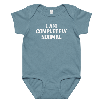 "I am completely normal" printed on a vintage indigo baby jersey bodysuit laying on a flat surface amongst other clothes