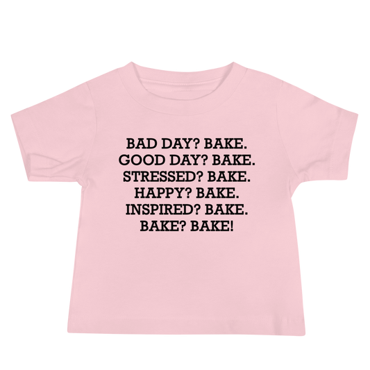 "Bad Day? Bake. Good Day? Bake. Stressed? Bake. Happy? Bake. Inspired? Bake. Bake? Bake!" printed on a pink baby jersey short sleeve tee laying on a flat surface