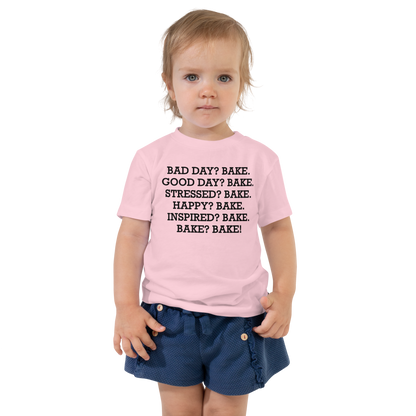 "Bad Day? Bake. Good Day? Bake. Stressed? Bake. Happy? Bake. Inspired? Bake. Bake? Bake!" printed on a pink toddler short sleeve tee worn by a female